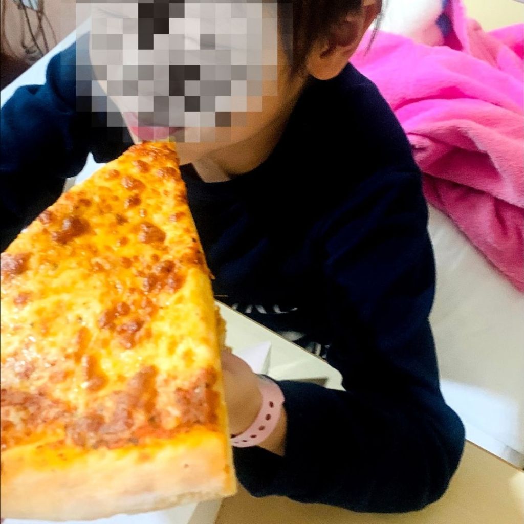 Fed is best. Child cancer patient eating pizza from her hospital bed. 